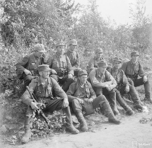 Mustavalkoinen kuvistuskuva. Miehet sodassa, istuvat tien penkalla.