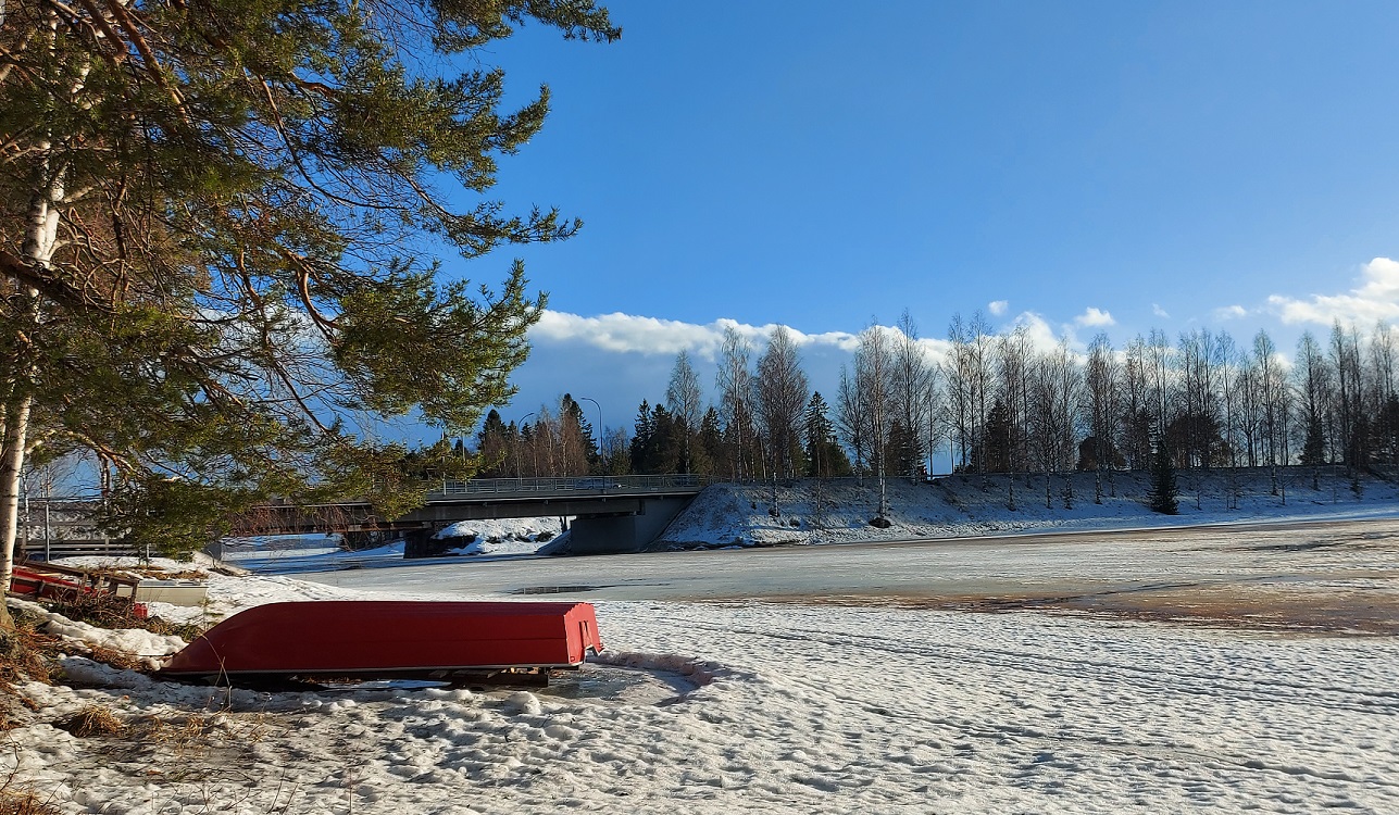 Taustakuva. Jäätyneen järven rannassa punainen vene kumollaan ja taustalla Mikonniemen silta. Kuvasta myös linkkejä kaupungin sivujen eri osioihin.